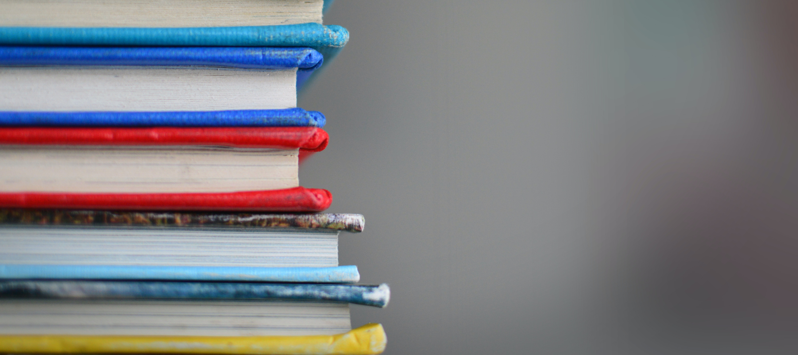 Stack of colorful hardcover books with blurred grey background